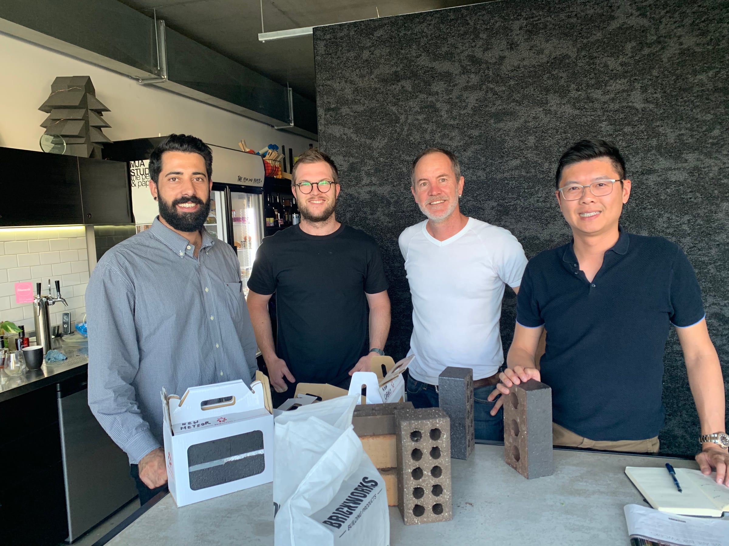 Four people at a studio kitchen bench with boxes of brick samples from Brickworks in front of them, smiling at the camera
