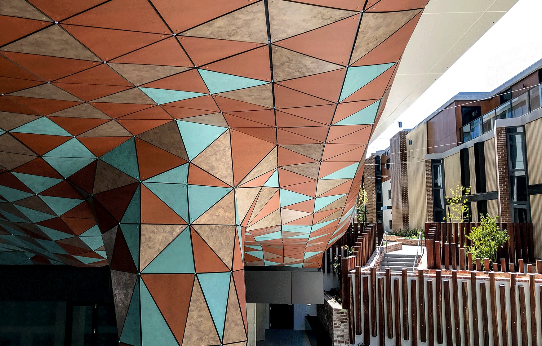 Sunlit view along Anemoi's copper and turquoise underbelly as it sweeps past balconies and a timber post fence