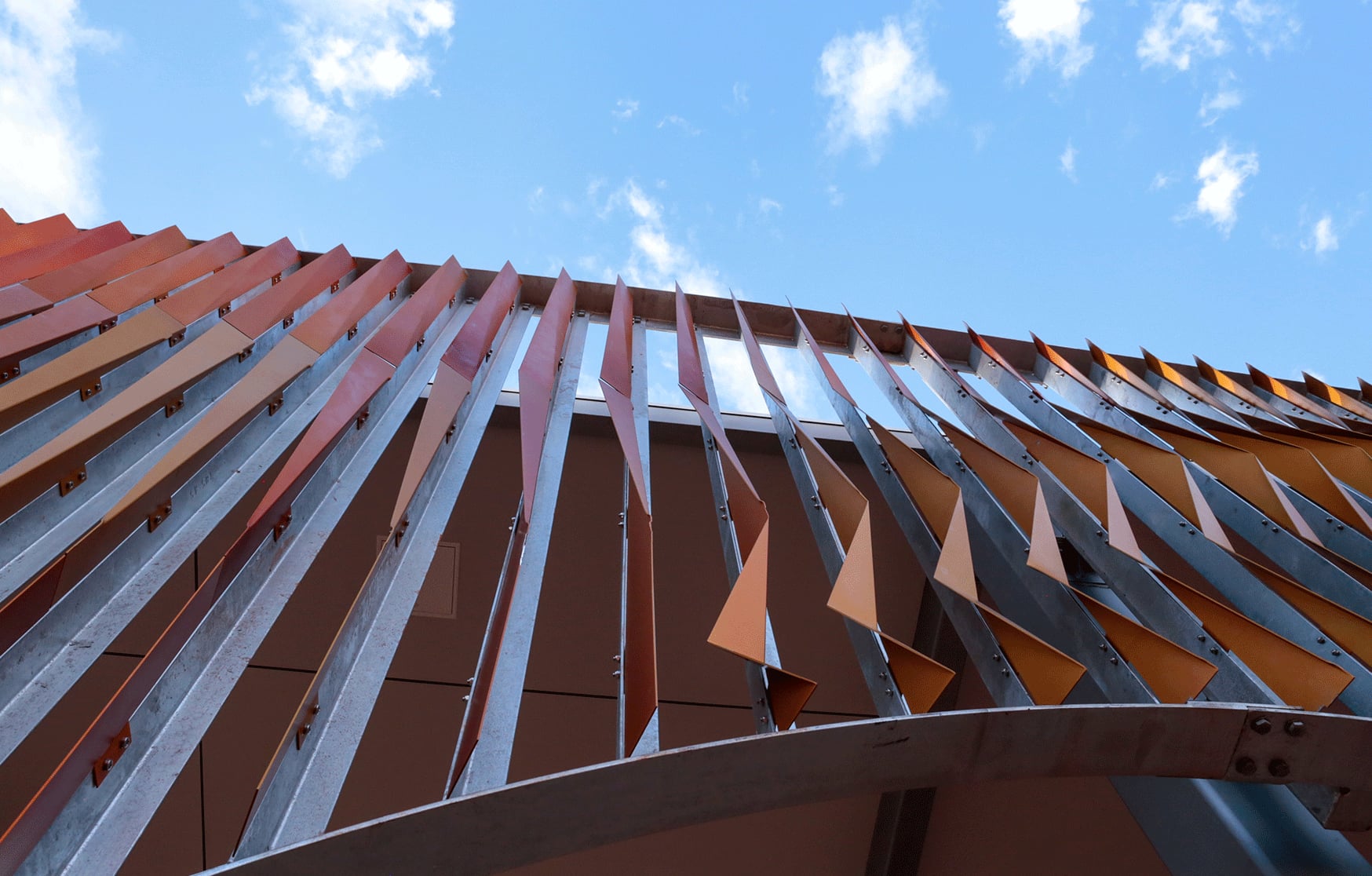 Looking up at the orange folded aluminium fins of Pleated Histories rippling against a Broome sky