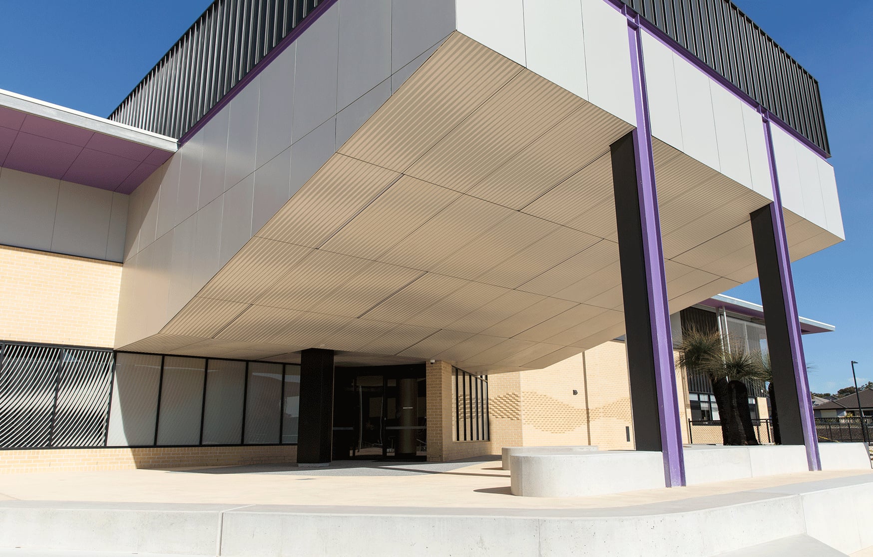 Looking up at the cantilevered college entry at Yanchep Secondary College, its CNC routered soffit striped between purple columns