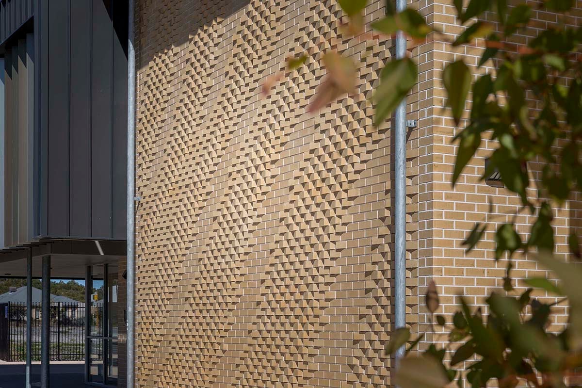 Afternoon light grazes the rotated brick artwork beside the glazed entry at Yanchep Secondary College.