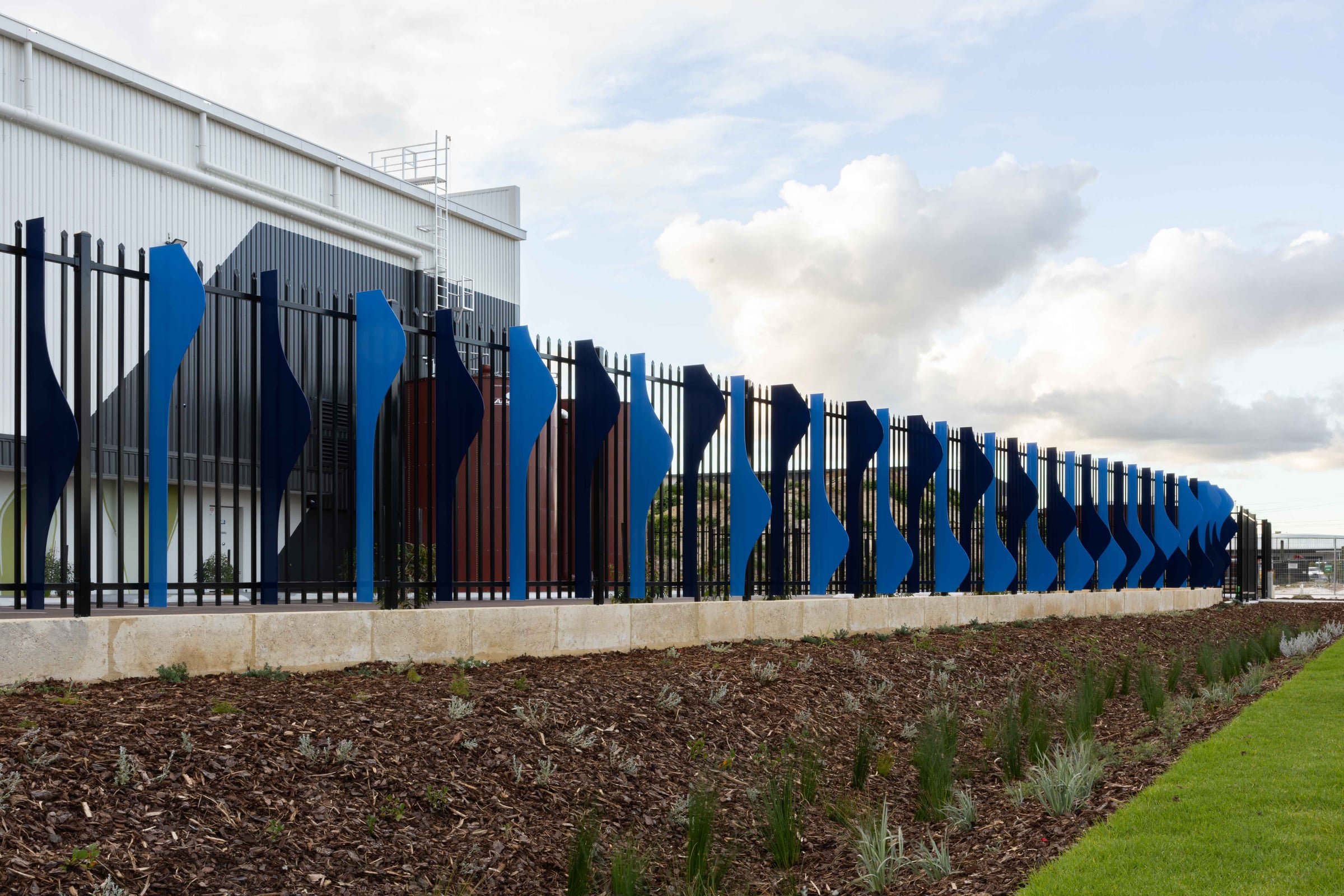 Rising from a limestone plinth, the blue aluminium fins of Cascading Creeks edge a native garden in Hazelmere.