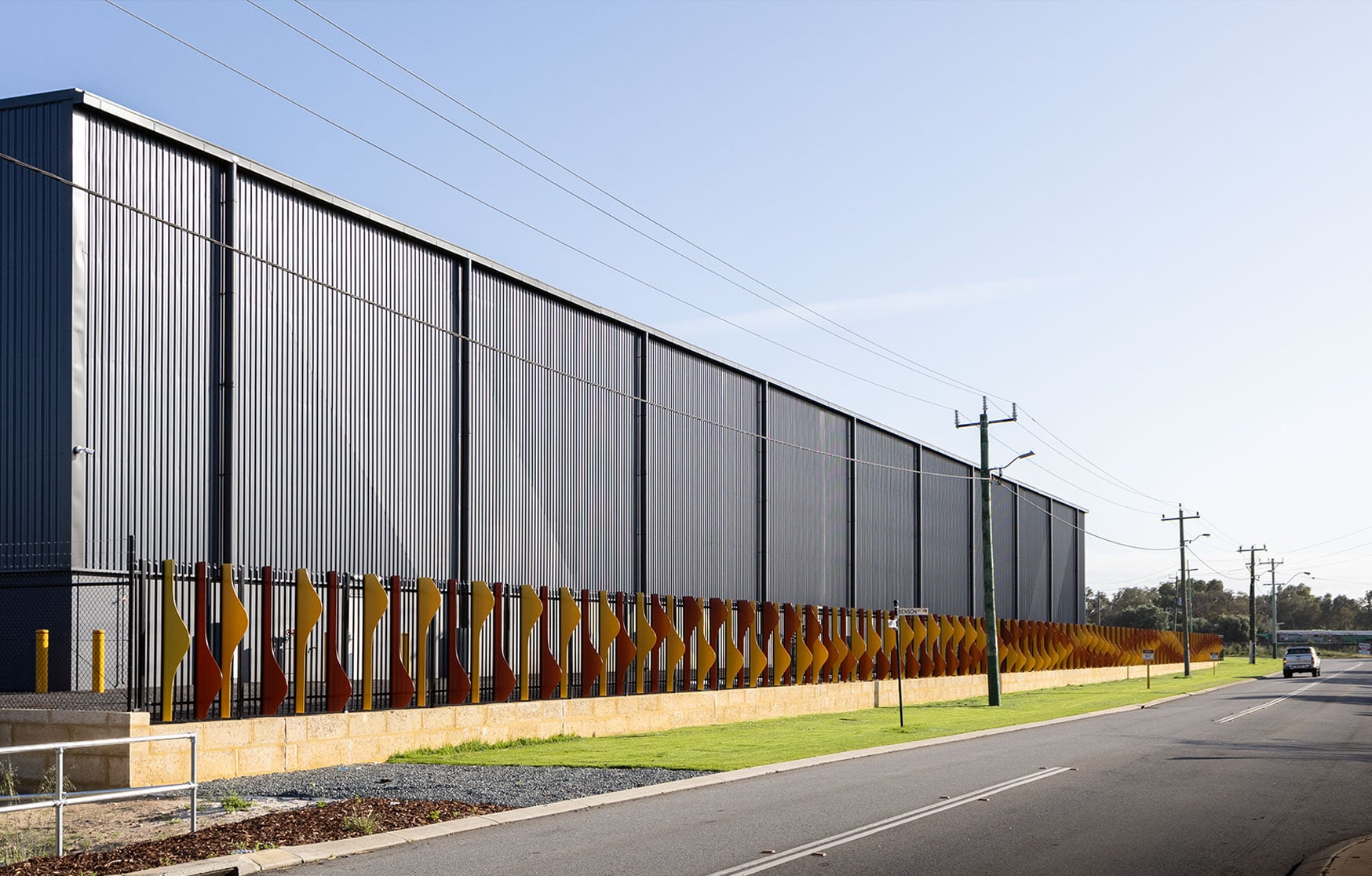 The gateway artwork wraps the warehouse corner, its red and gold fins seen from the road in Hazelmere.