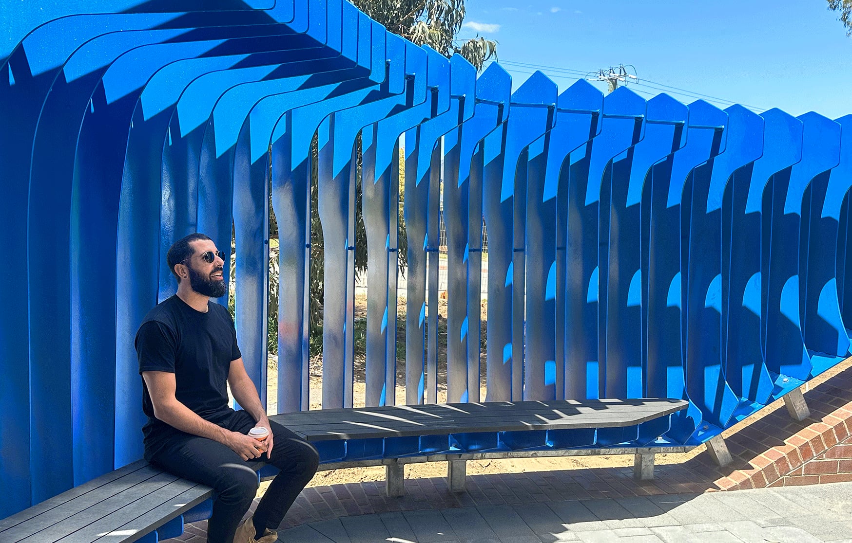 A visitor rests on the composite bench inside the sweeping blue painted steel fins of The Exchange at Carine SHS.