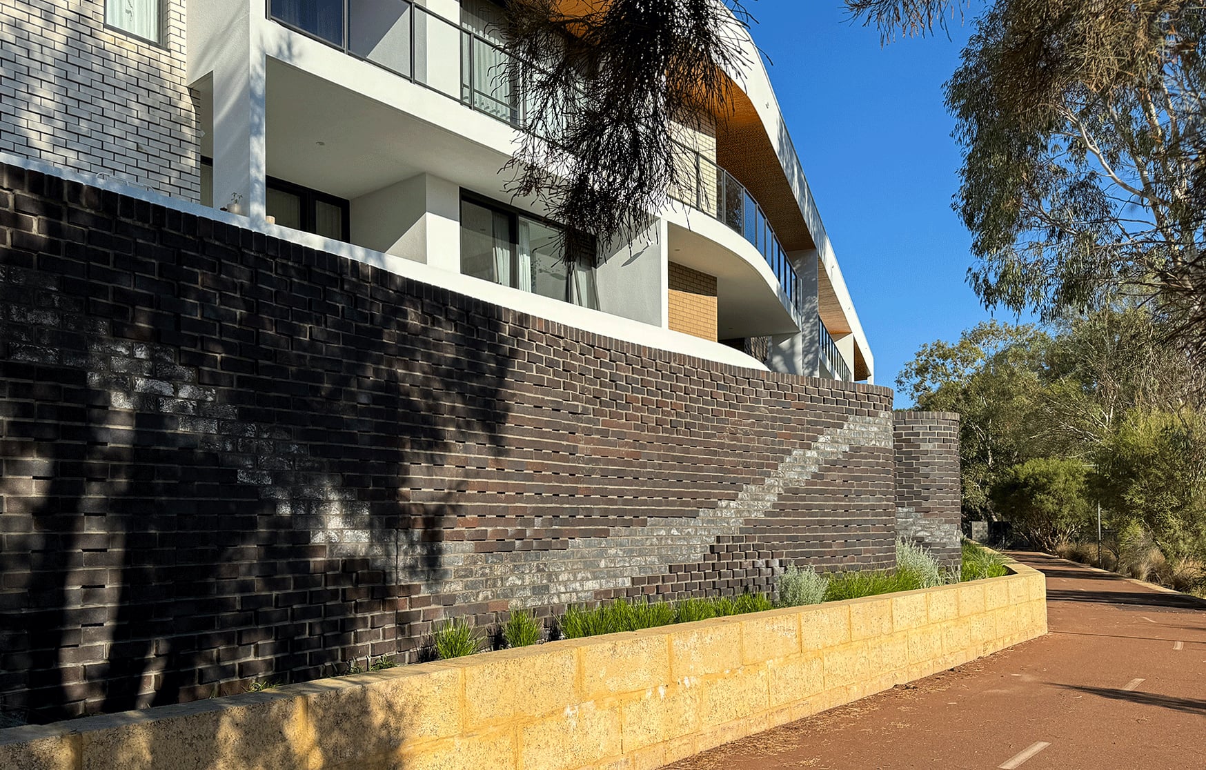 Glazed and matte bricks trace a diagonal current across the Waterford wall above a limestone planter