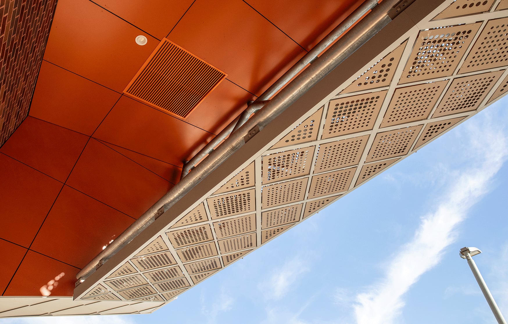 Where the orange soffit meets the perforated diamond band, custom brackets tilt each panel toward the sky