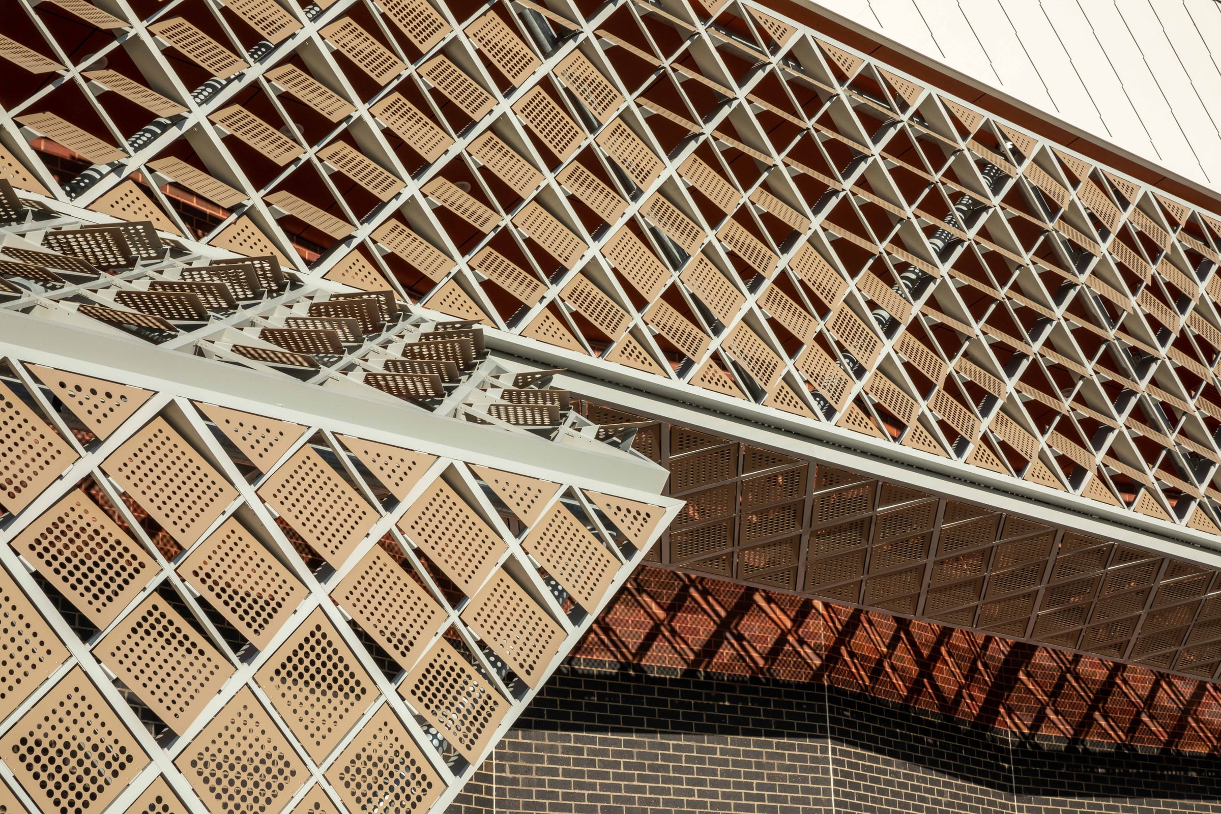 Two wings of the perforated screen cross in warm light, casting diamond shadows on the brick below