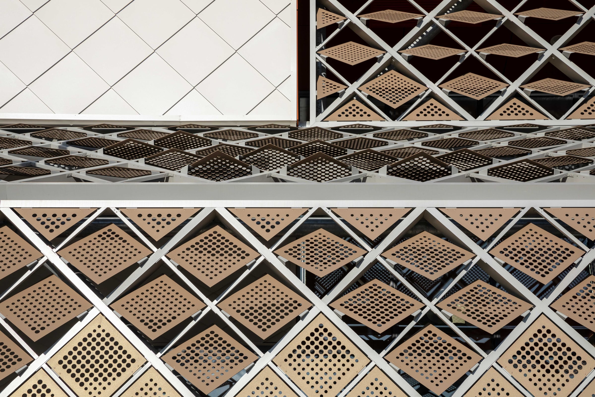 Flat on view of the facade layers, white shingles above and rows of tilted perforated panels below