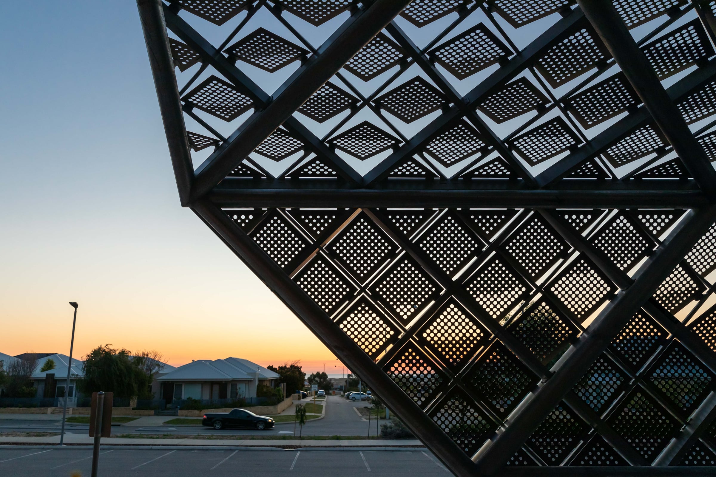 Sunset glows through the perforated panels of Windswept, each rotated square reading as a pixel of coastal light