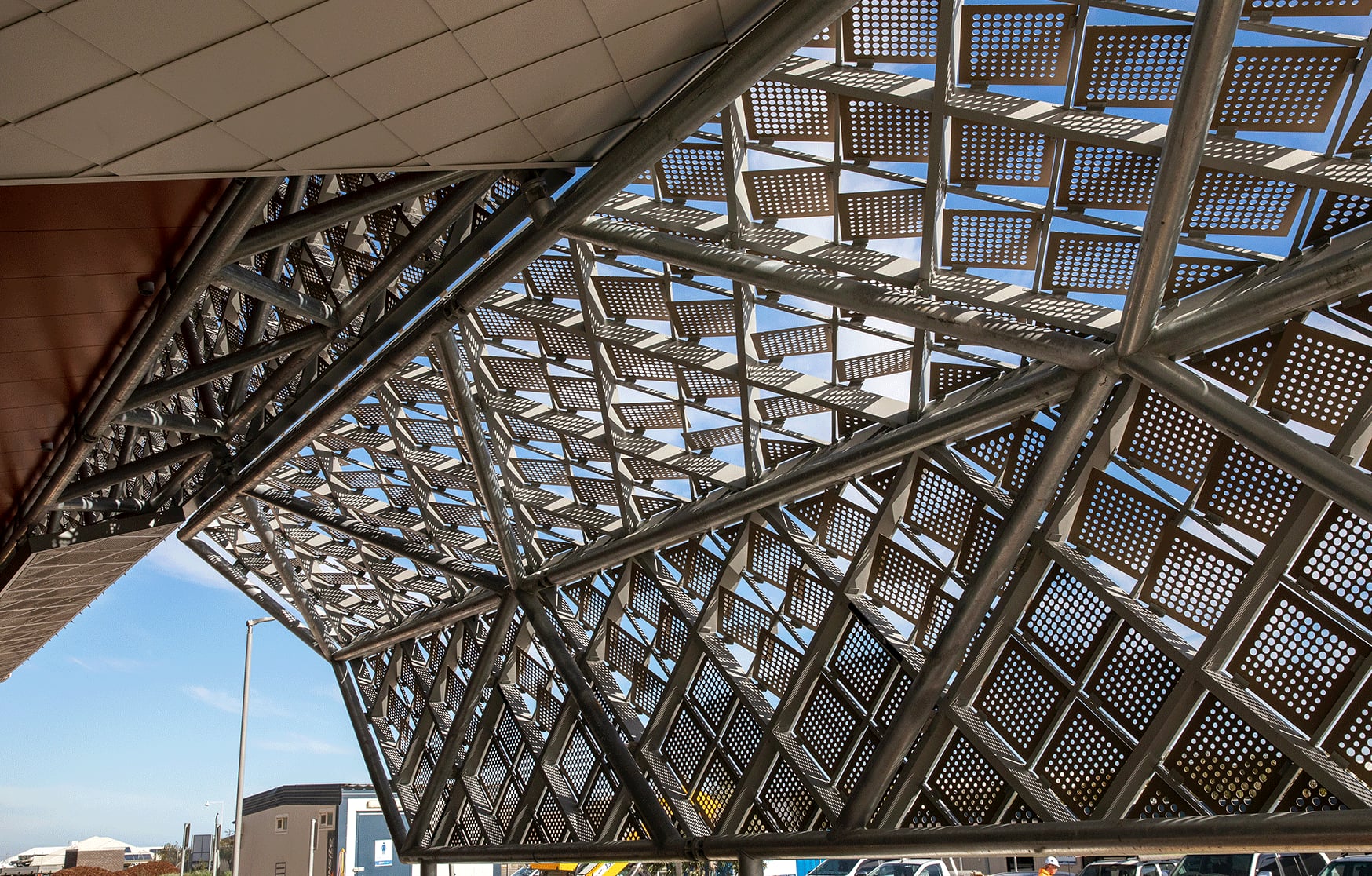 Looking out from under the tilted canopy, rotated perforated squares hover on their galvanised space frame